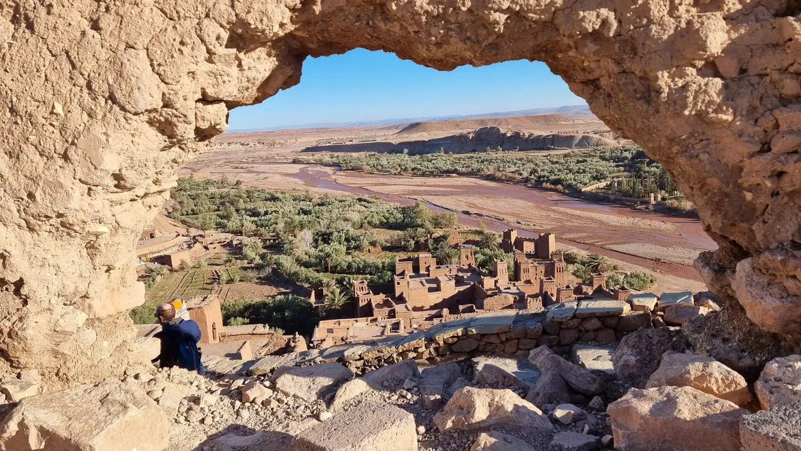 Maisons en terre, palmeraie et lit de l'oued vus à travers une arche rocheuse dans le Sud marocain