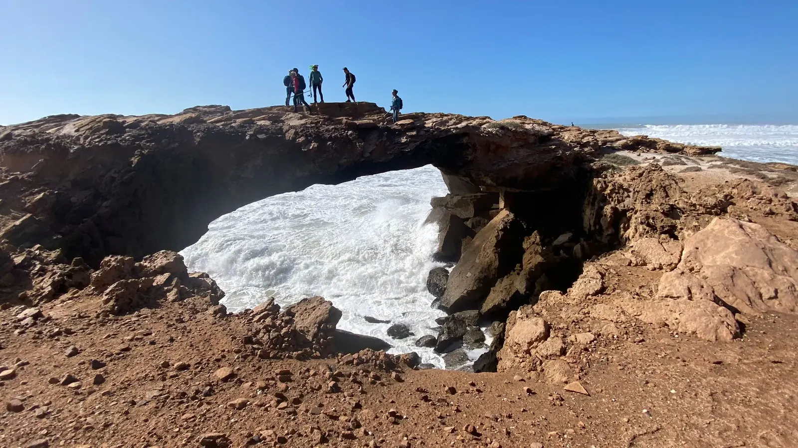 Senderistas sobre un arco de roca formado por el océano en un acantilado de la costa atlántica de Marruecos