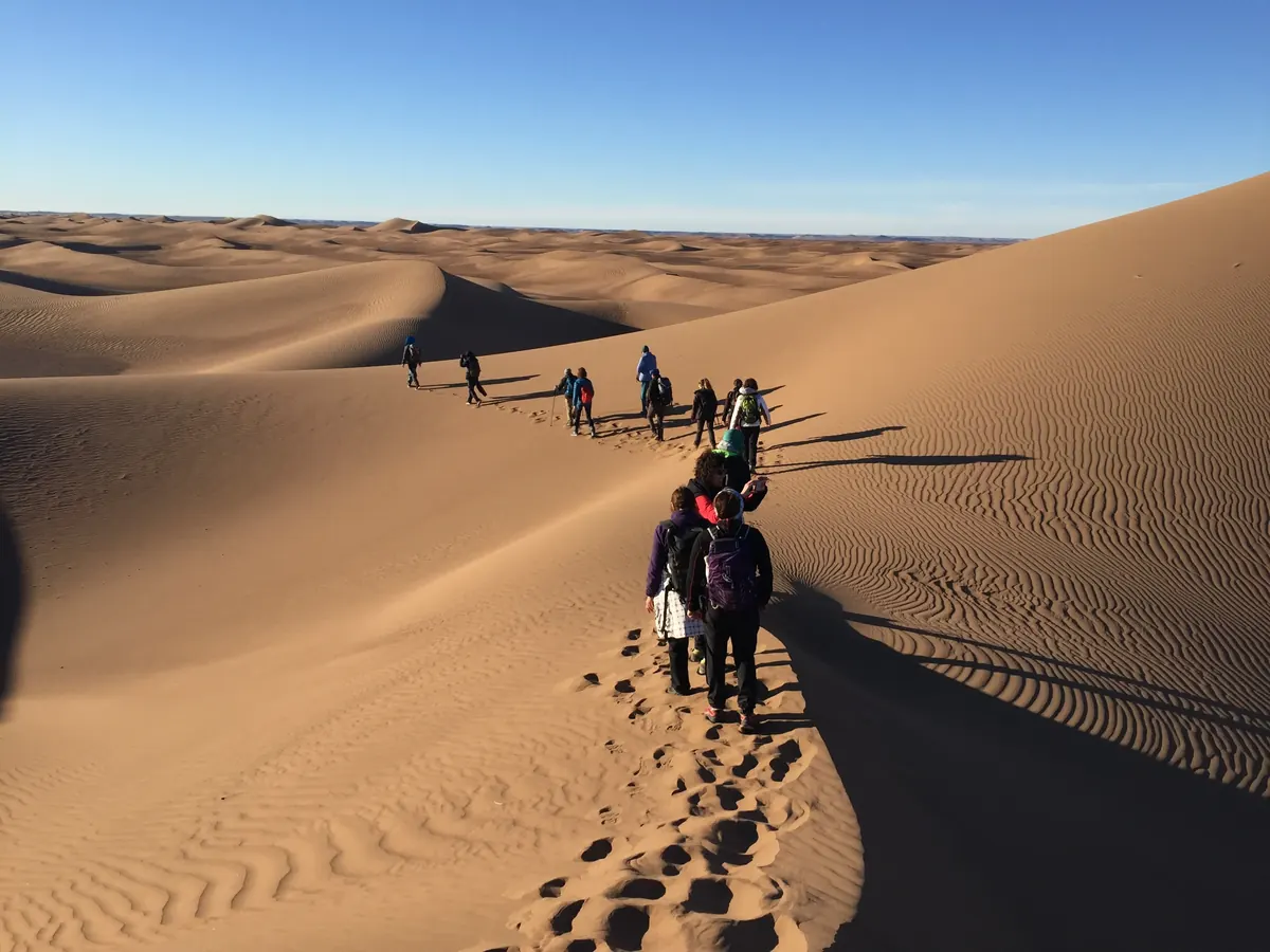 Grupo de senderistas bajando en fila por la arista de una duna en el desierto de Marruecos