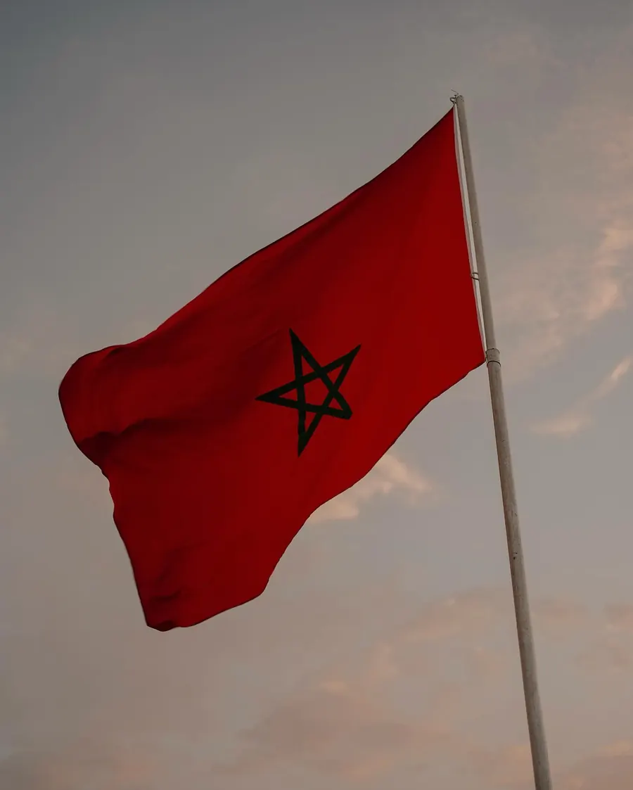 Bandera de Marruecos roja con la estrella verde entrelazada ondeando en un mástil al atardecer