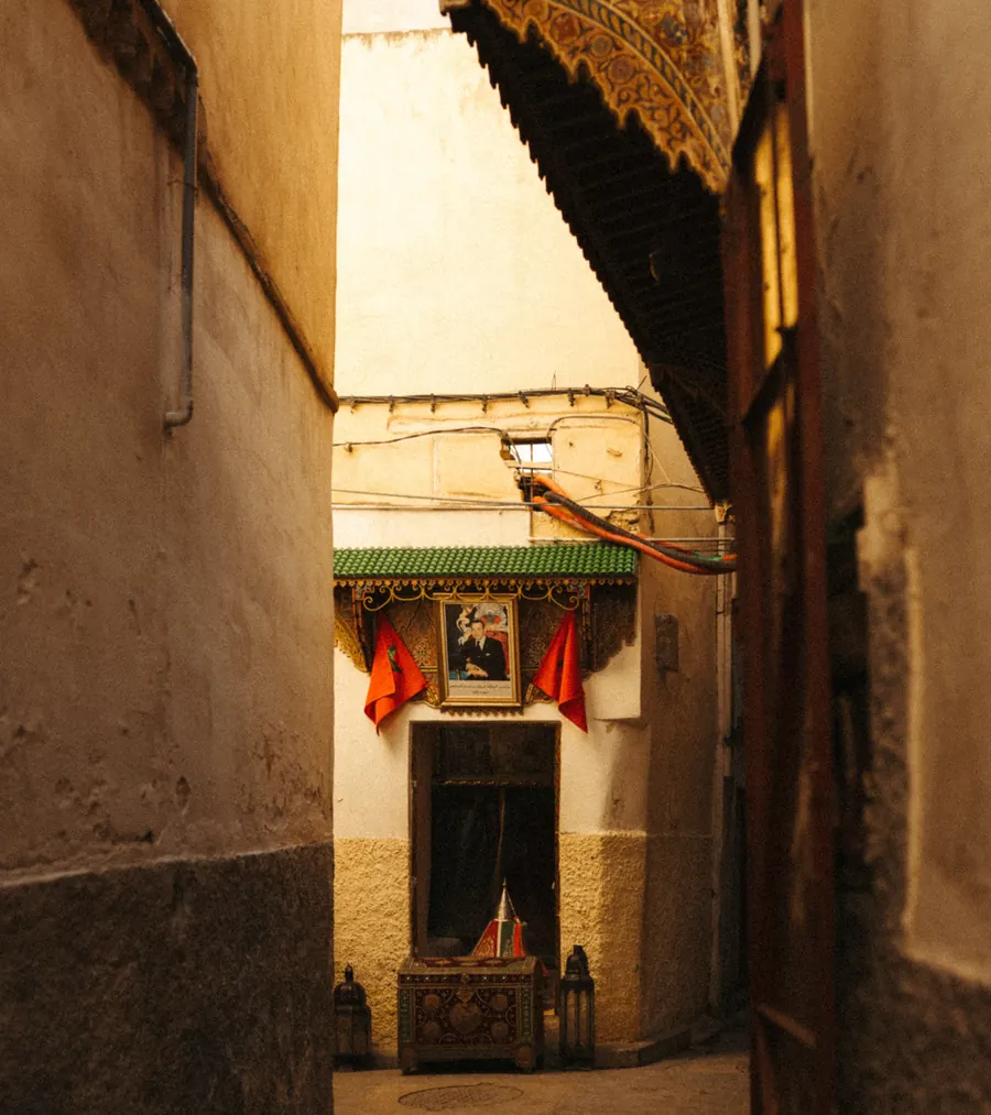 Dos banderas de Marruecos a ambos lados de un retrato real sobre una puerta en un callejón de la medina