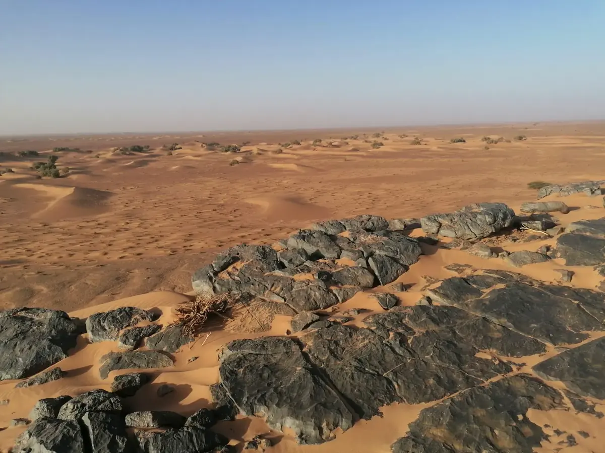 Black rock outcrop half covered by sand, with dunes beyond, in the Moroccan Sahara