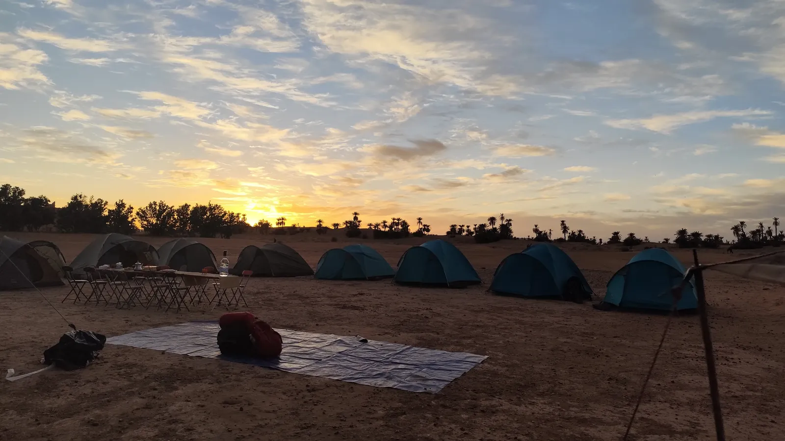 Campamento con tiendas en el desierto de Marruecos al amanecer, junto a un palmeral