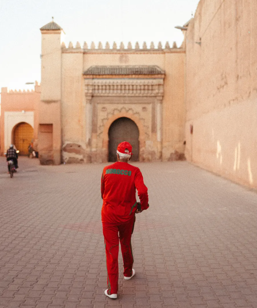 Hombre con chándal rojo y la palabra MOROCCO en verde en la espalda caminando por una ciudad antigua