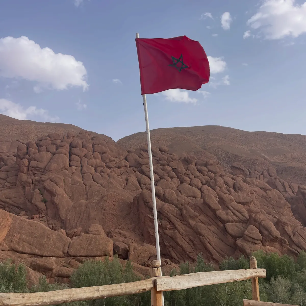 Drapeau marocain en haut d'un mât devant une falaise de roches rouges arrondies sous un ciel bleu