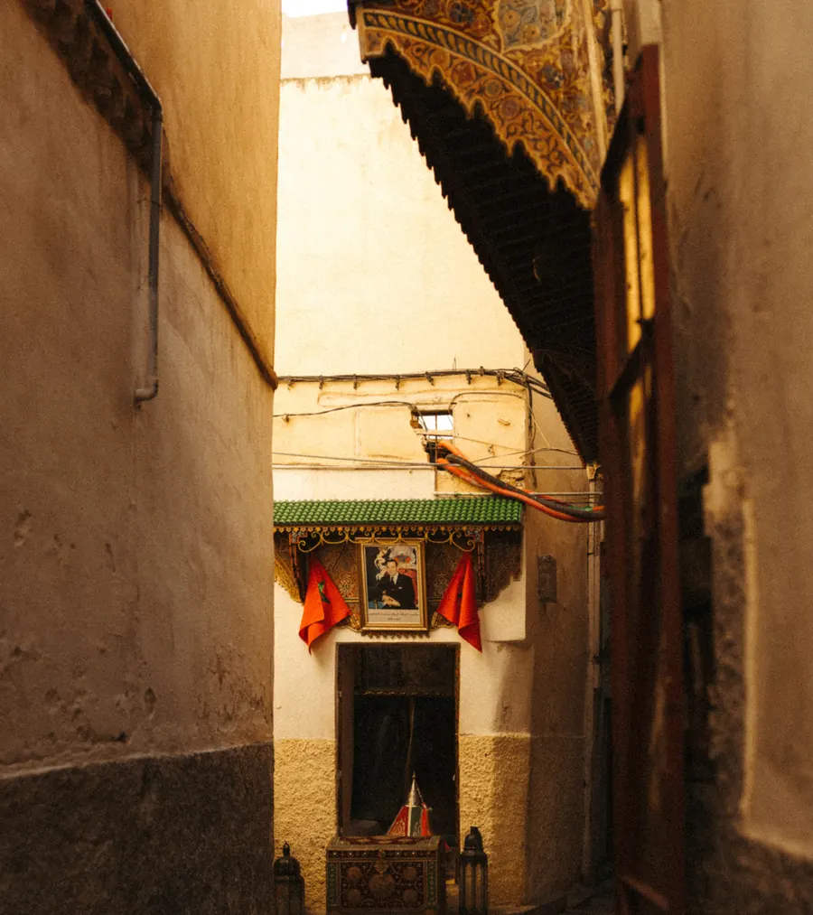 Deux drapeaux marocains de part et d'autre d'un portrait royal au-dessus d'une porte dans une ruelle de médina