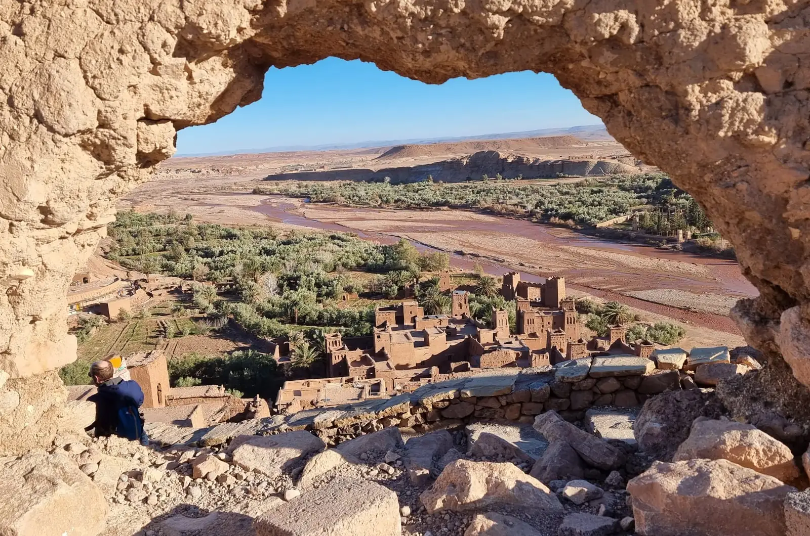 Earthen houses, palm grove and riverbed seen through a rock arch in southern Morocco