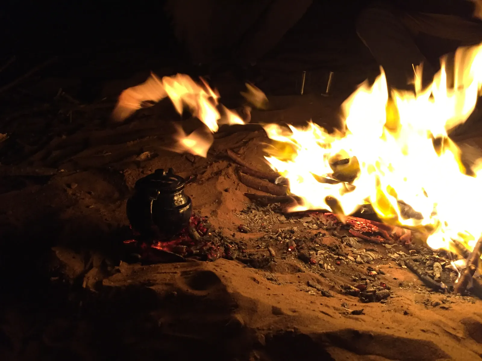 Fuego de campamento con una tetera en las brasas durante la noche en el desierto