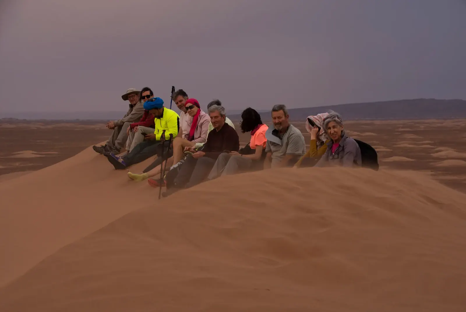 Grupo de senderistas descansando en lo alto de una duna bajo un cielo gris en el desierto de Marruecos