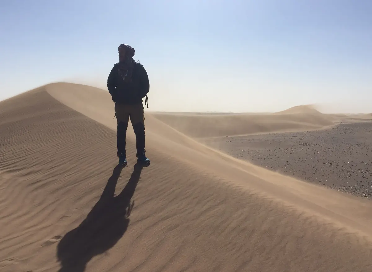 Hiker standing on a dune crest in strong wind and hazy light in the Moroccan desert