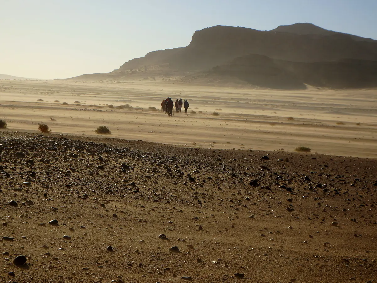 Group of hikers walking across a gravel plain towards a flat-topped mesa in the Moroccan desert