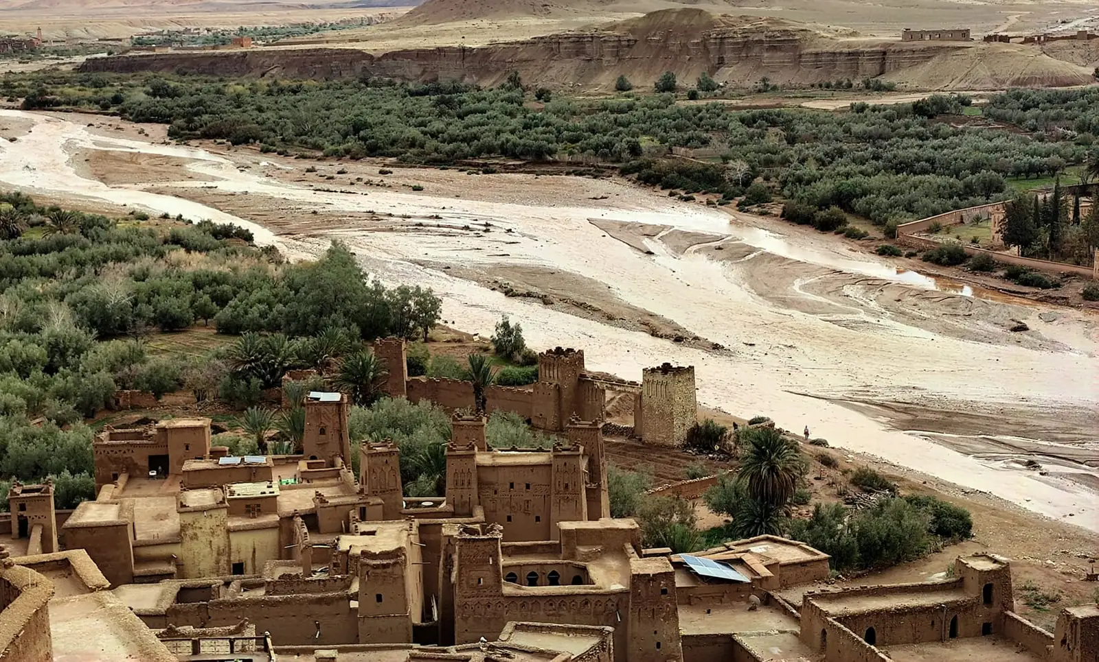 Maisons et tours en terre au bord d'une palmeraie et du large lit d'un oued dans le Sud marocain