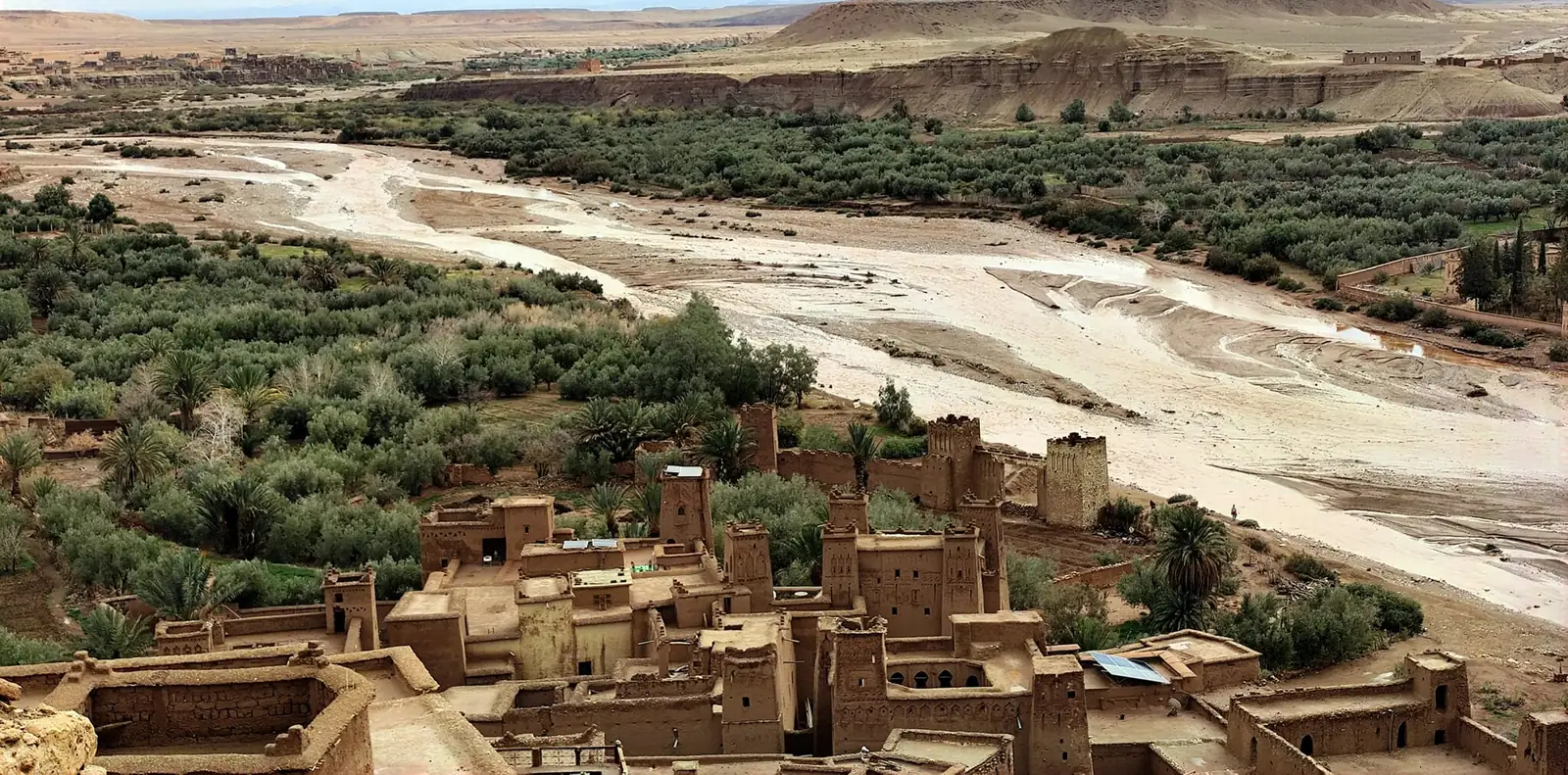 Earthen houses and towers beside a palm grove and a wide riverbed in southern Morocco