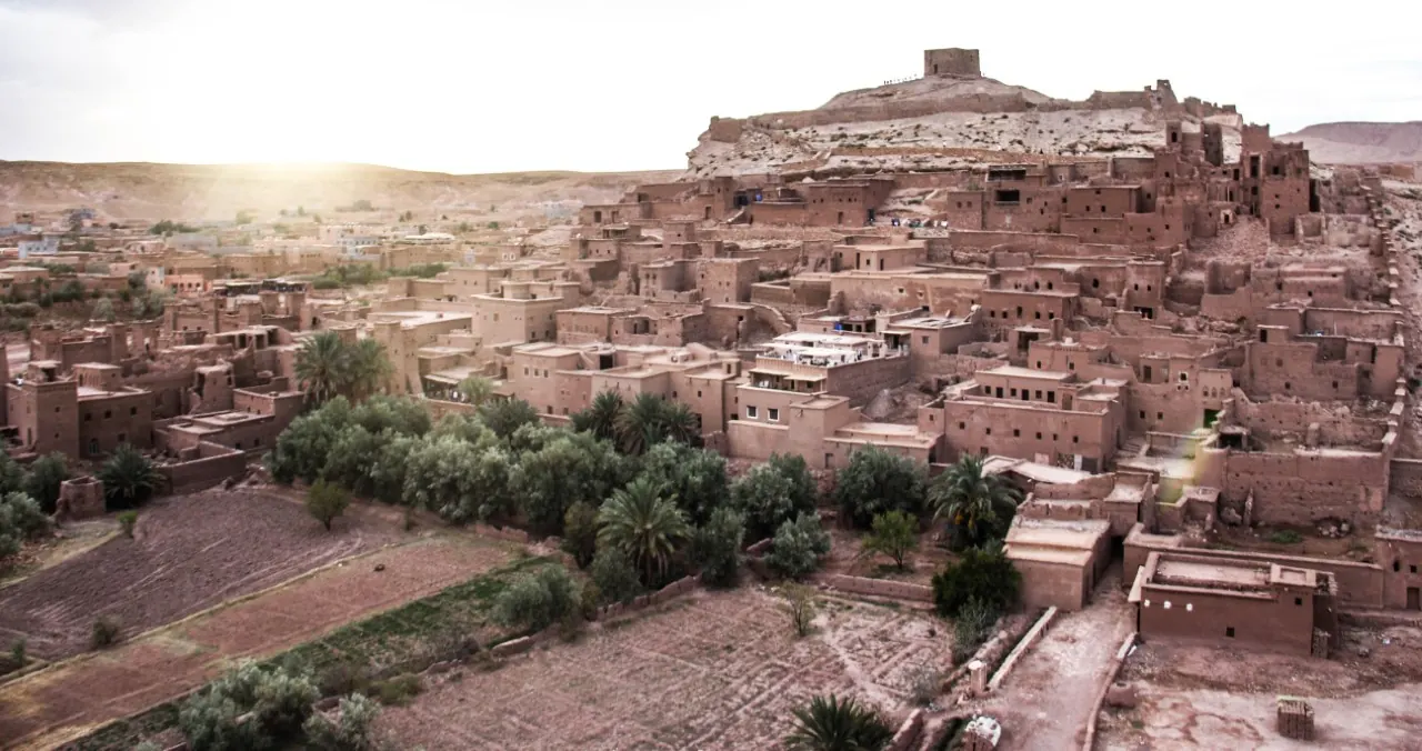 Ksar d'Aït Ben Haddou sur sa colline, avec ses maisons en terre, palmiers et jardins au pied, au coucher du soleil