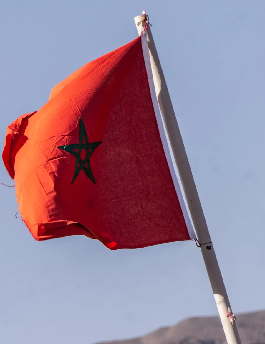 Moroccan flag flying from a white pole against a pale sky with bare mountains below