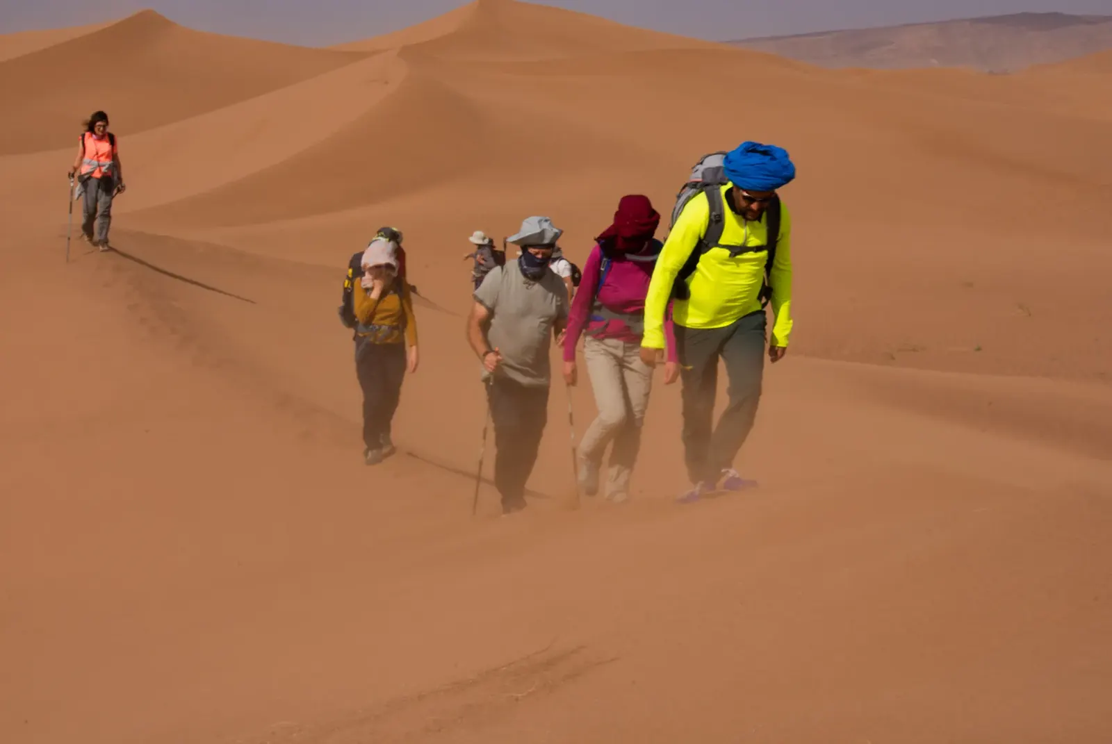 Groupe de randonneurs marchant dans les dunes par vent de sable, désert marocain