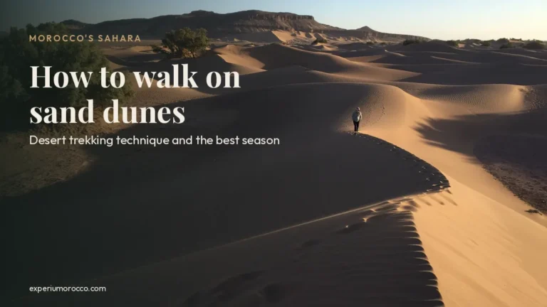 A lone hiker walking along the shaded ridge of a sand dune in Morocco's Sahara, with mountains behind