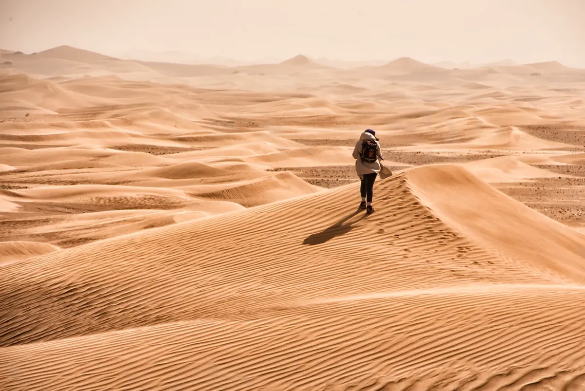 Senderista caminando entre las dunas con el aire cargado de polvo en el desierto de Marruecos