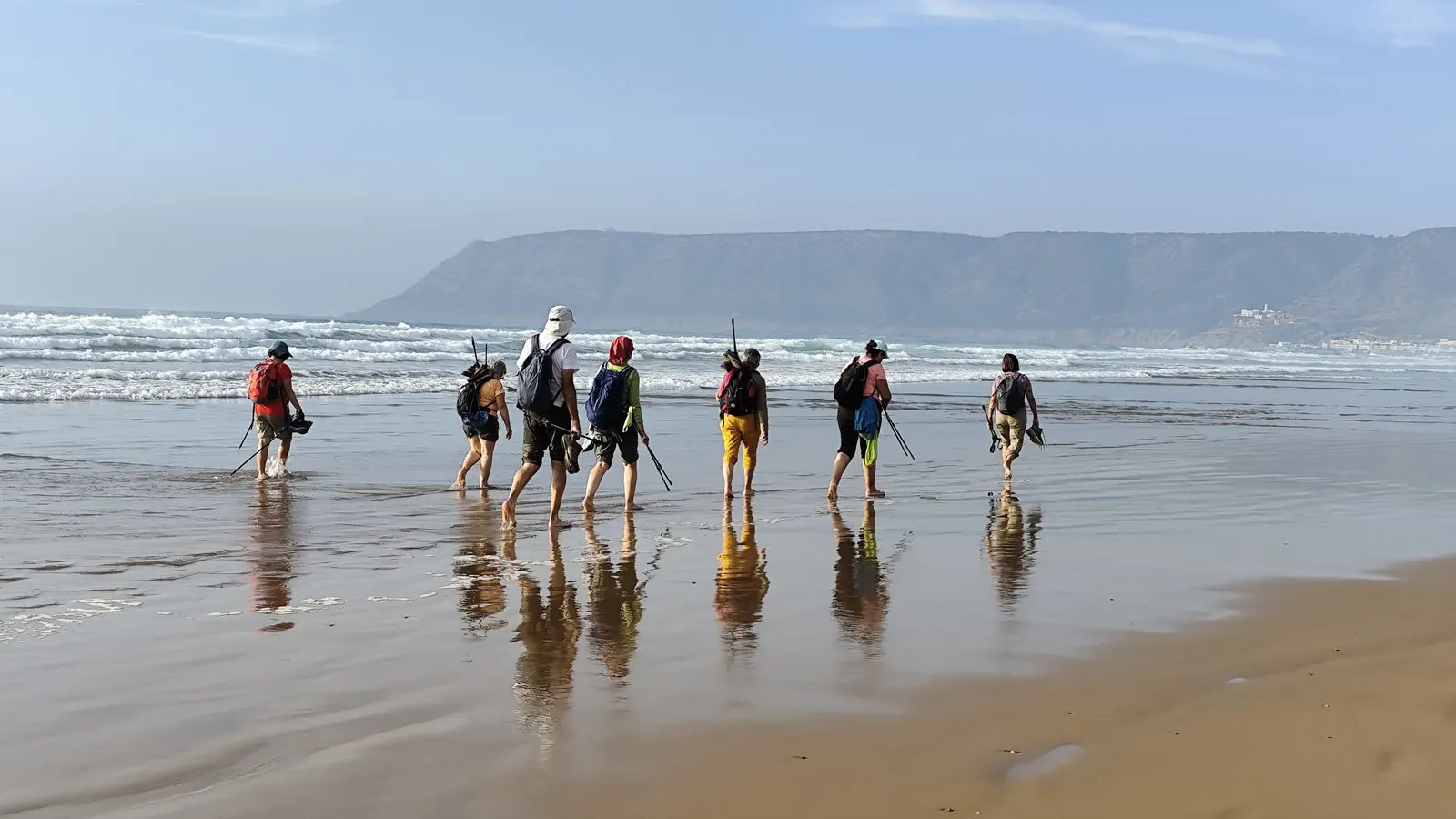 Grupo de senderistas caminando por la arena húmeda con la marea baja en una playa del Atlántico, Marruecos