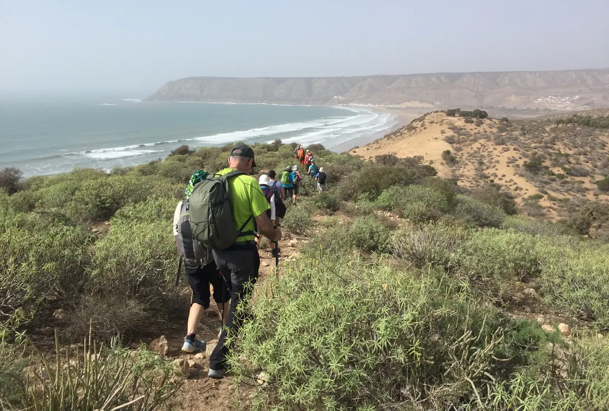 Senderistas bajando por un sendero entre matorral hacia el océano Atlántico en Marruecos