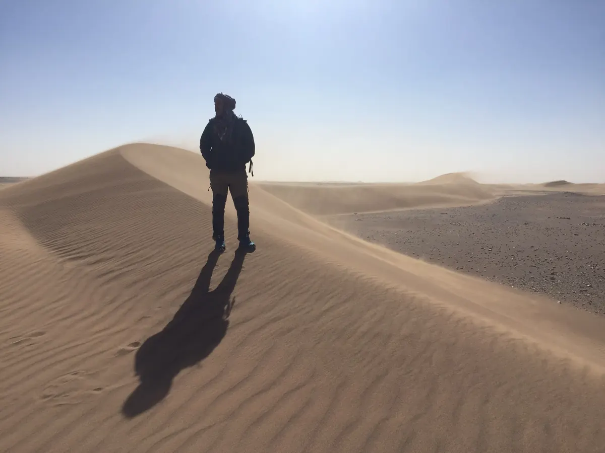 Silhouette d'un randonneur sur une crête de dune balayée par le vent dans le désert marocain