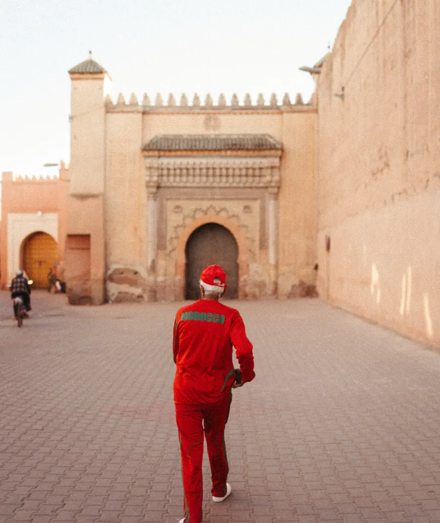 Homme en survêtement rouge avec MOROCCO écrit en vert dans le dos, marchant dans une vieille ville