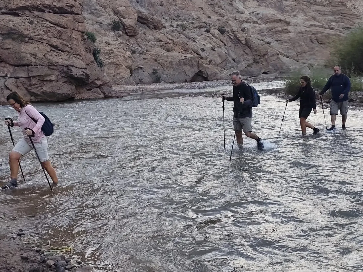 Groupe de randonneurs traversant une rivière à gué avec des bâtons pendant un trek au Maroc
