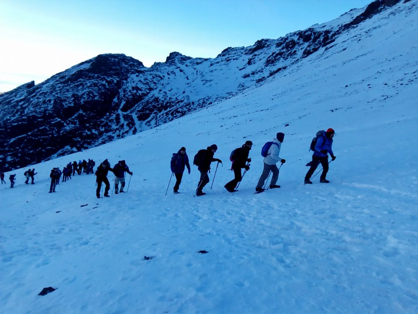 Groupe de randonneurs montant en file une pente enneigée avec des bâtons en haute montagne au Maroc