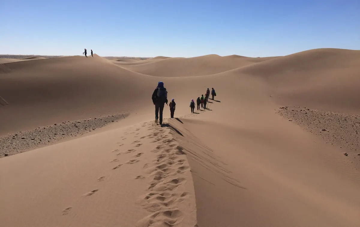 Grupo de senderistas en fila por la cresta de una duna durante un trekking por el desierto de Marruecos