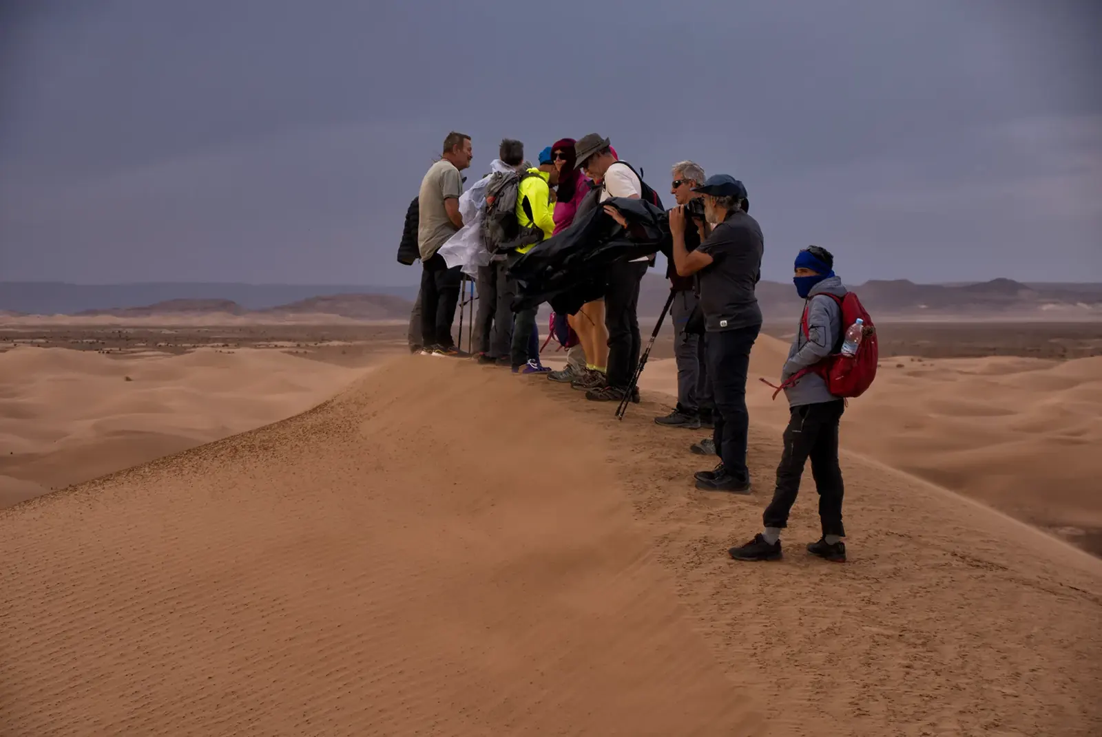 Group of hikers on top of a sand dune under a stormy sky in the Moroccan Sahara