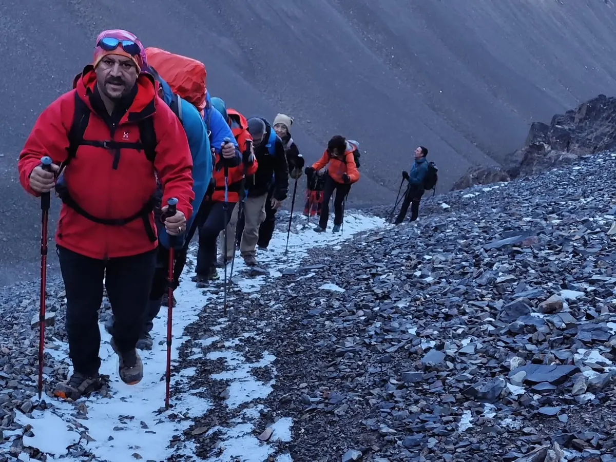 Trekkers with telescopic poles climbing in single file on a rocky trail with patches of snow