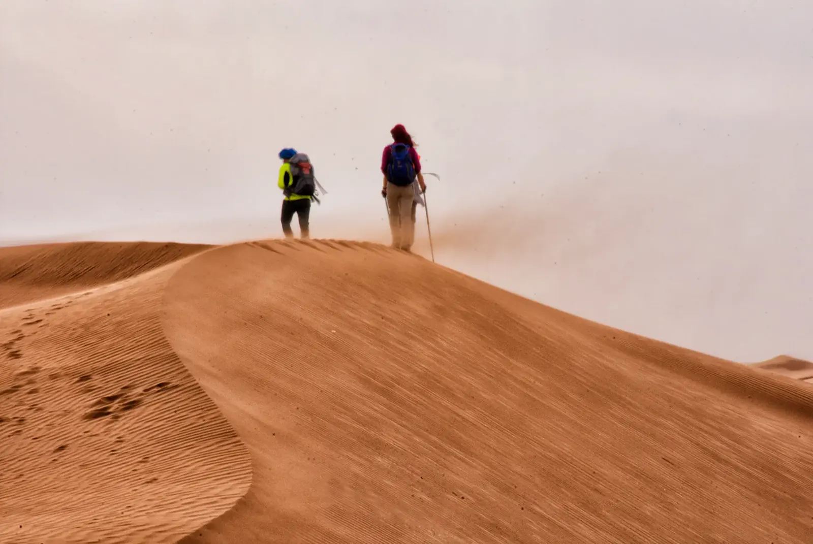 Dos senderistas en la cresta de una duna mientras el viento levanta la arena, desierto del Sáhara en Marruecos
