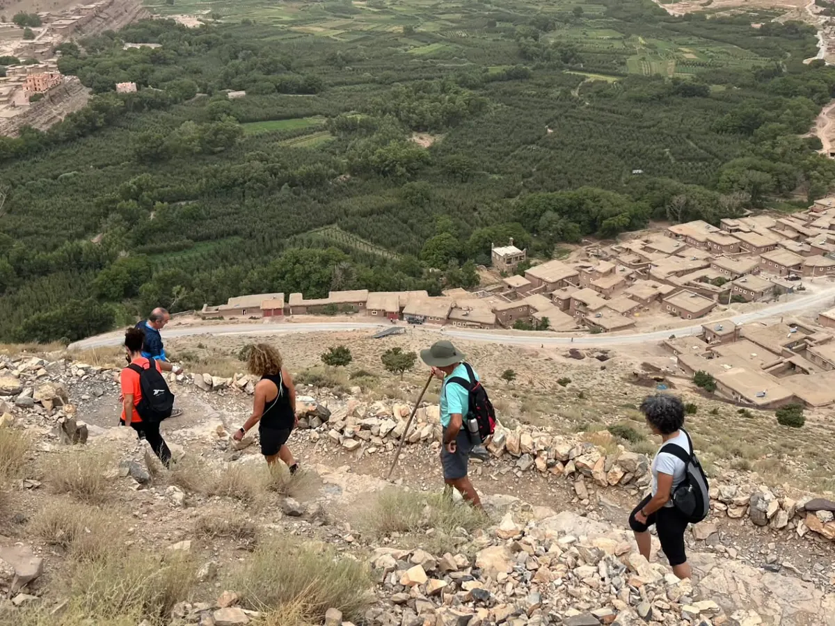 Trekkers walking down a stone path towards a mud-brick village and a green valley in Morocco