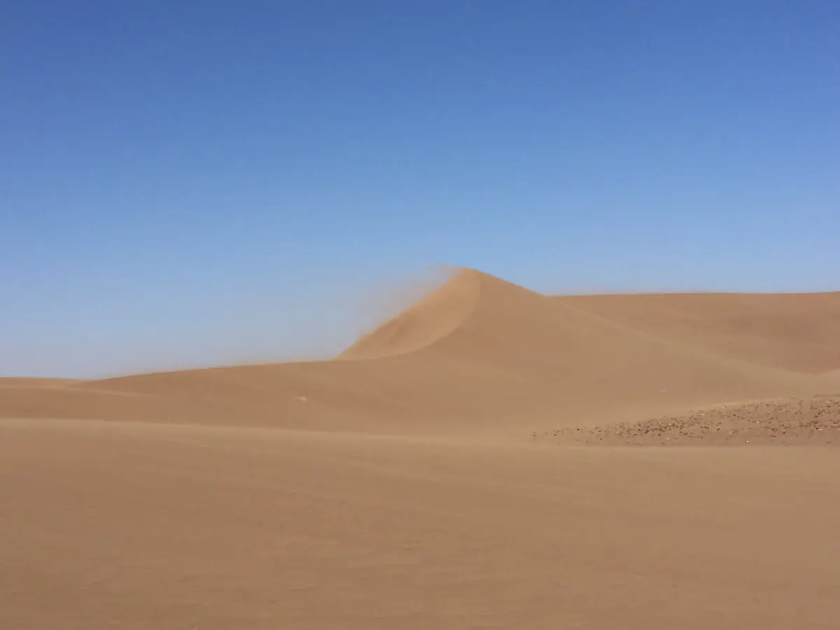 El viento arranca la arena de la cresta de una duna bajo un cielo azul en el Sáhara marroquí